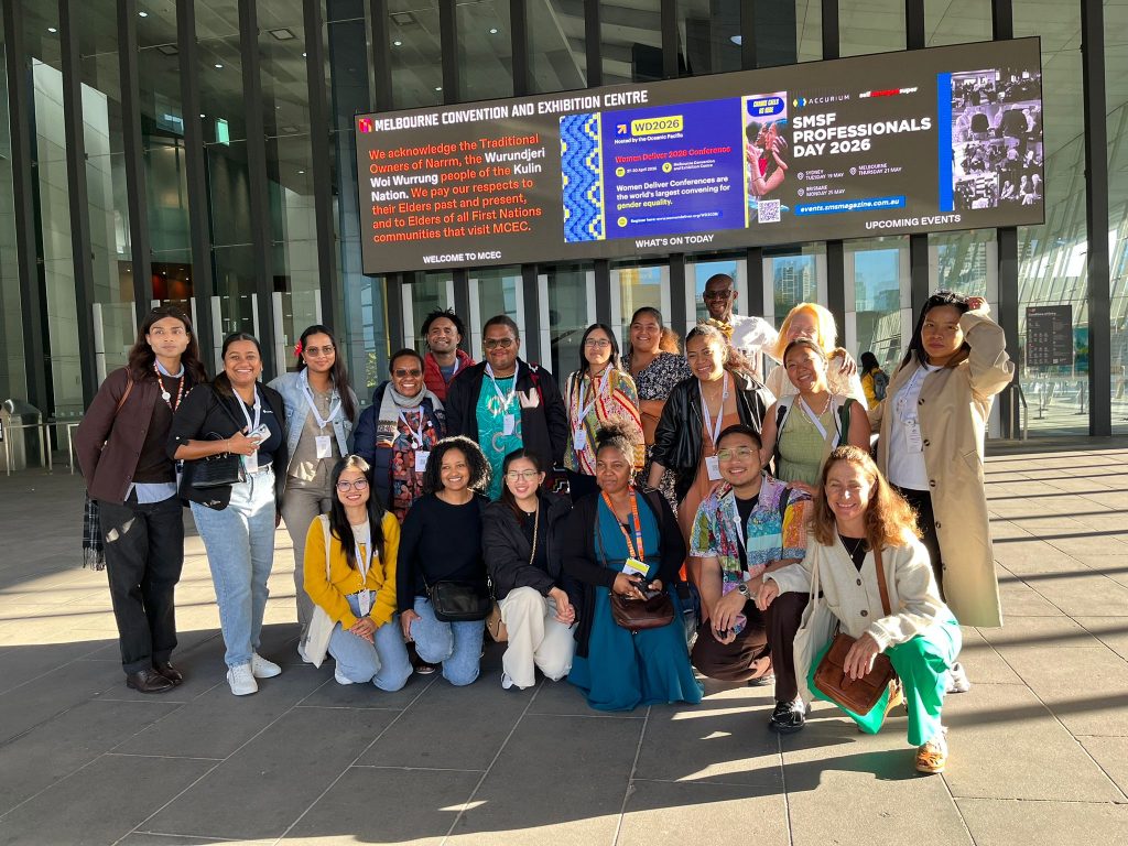 Participants group together crouching and standing at the entrance to the Melbourne Exhibition Centre. 