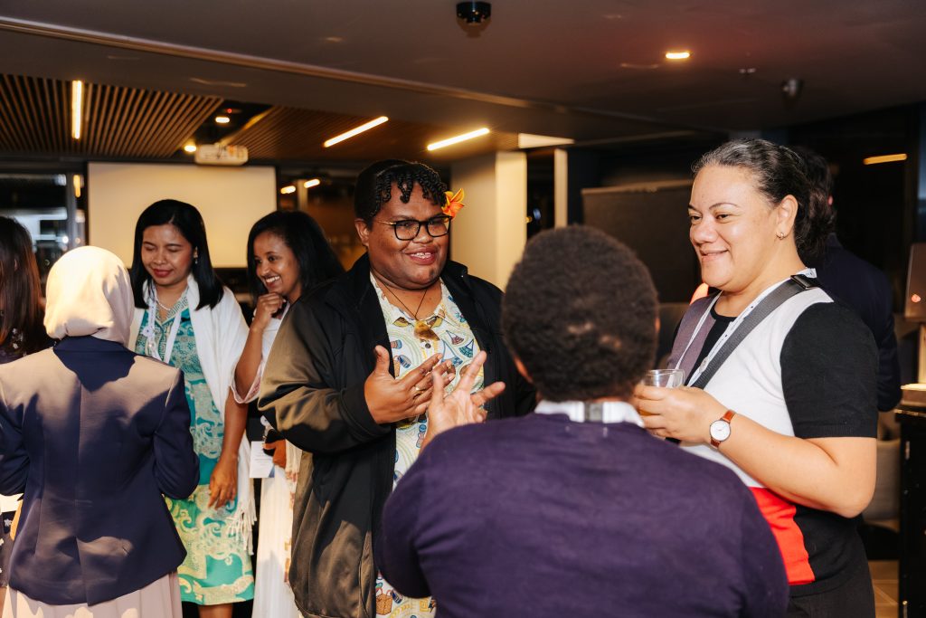 Mele talks with Women Deliver 2026 participants inside at a networking event.