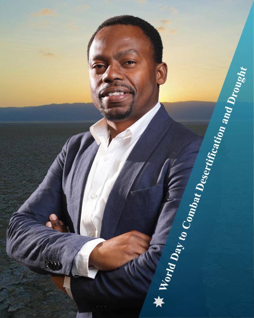 Alcino stands with his arms crossed smiling and wearing a blue suit with white shirt. There is a dry desert scene behind him with a setting sun and text: World Day to Combat Desertification and Drought.